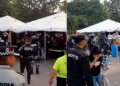 Crowd Under White Tents with Uniformed Security Personnel Monitoring an Outdoor Event Area. - Vecinos Unidos