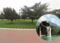 Park with green grass and trees; circular inset shows a rusted water chute pouring into a pool with mountains in the background.