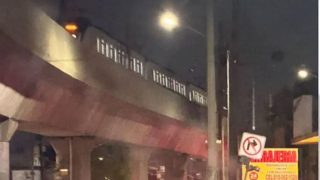 Nighttime Street Scene with an Elevated Rail/bridge Above a Storefront; a No-left-turn Sign is Visible on a Pole. - Vecinos Unidos